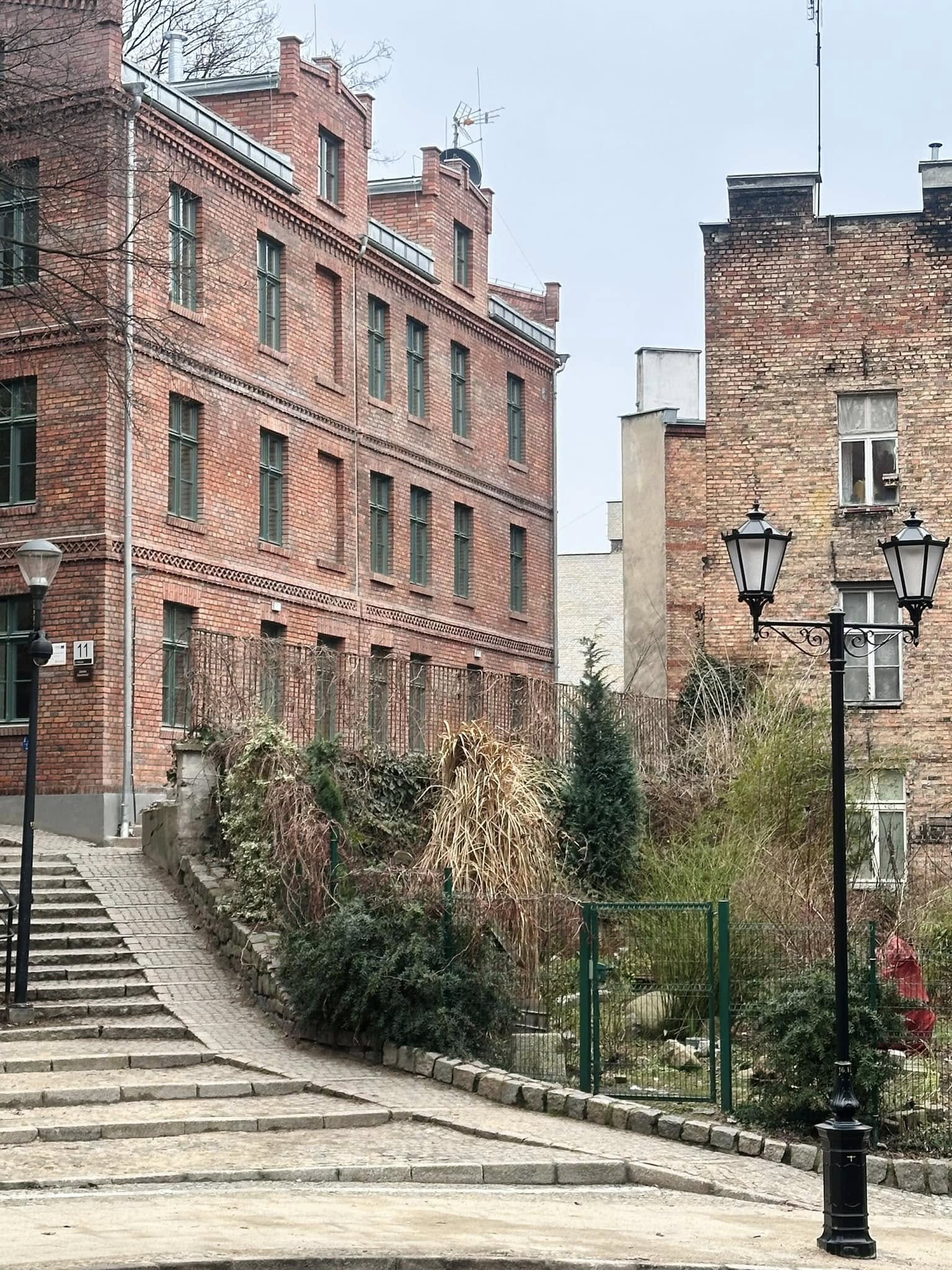 Zdjęcie przedstawia wyremontowaną kamienicę przy ul. Biskupiej 11 oraz sąsiedni budynek. Na pierwszym planie widoczne są również lampy uliczne