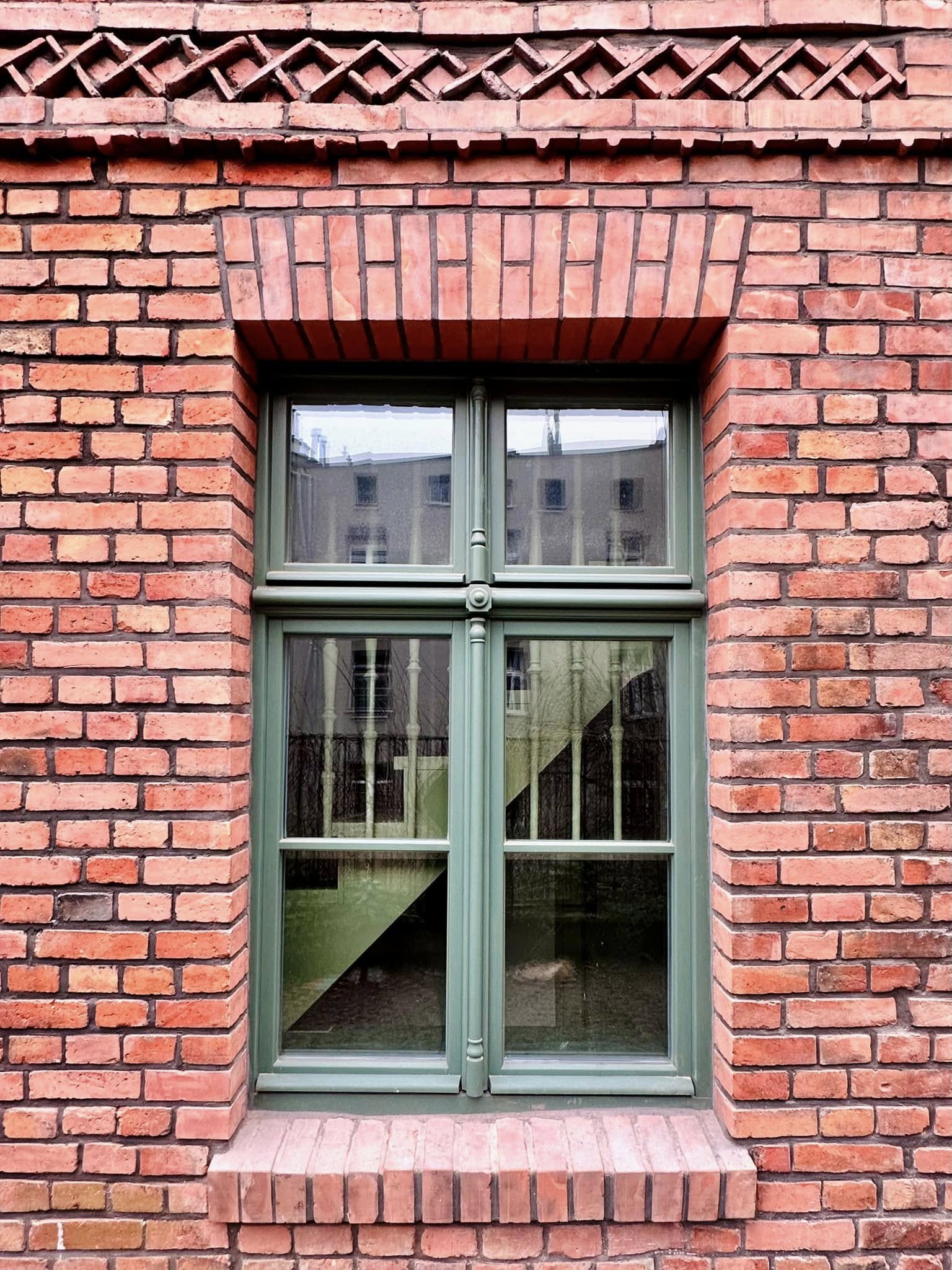 Zdjęcie przedstawia ceglaną elewację budynku oraz zielone okno