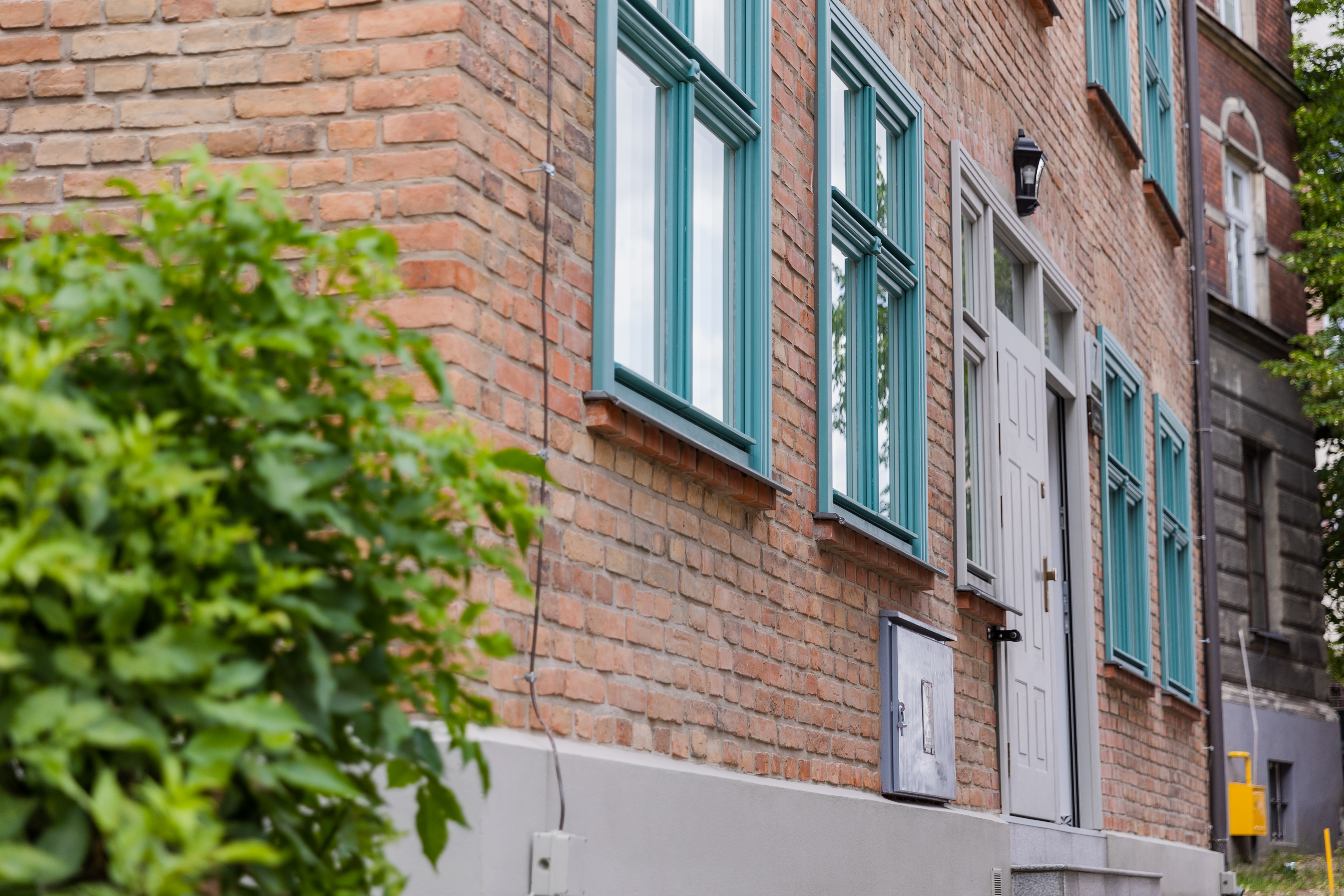 Zdjęcie przedstawia ceglaną elewację frontową budynku po modernizacji przy ul. Salwator 7 wraz z nową stolarką okienna i drzwiową w odcieniach błękitu