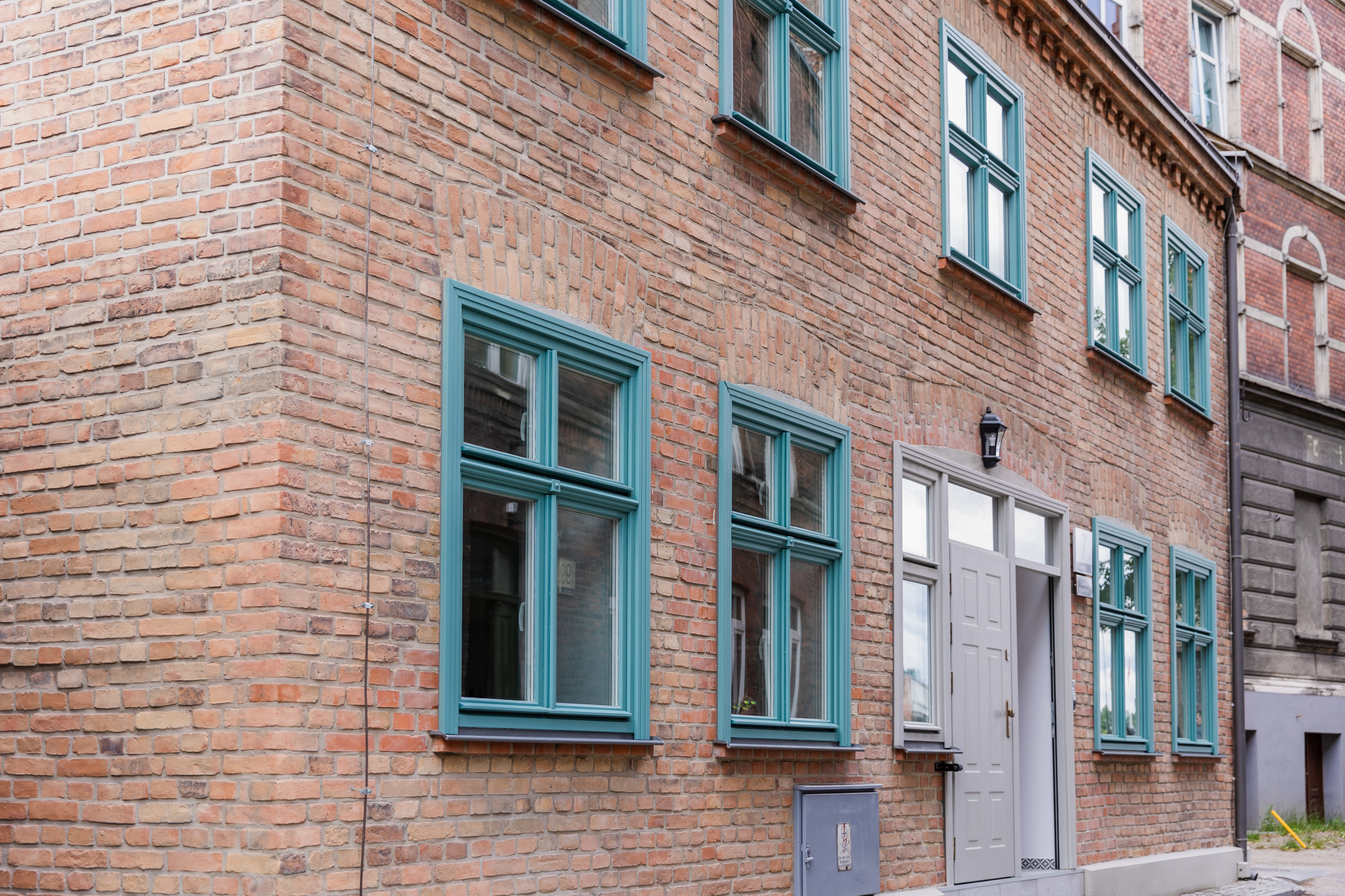 Zdjęcie przedstawia ceglaną elewację frontową budynku po modernizacji przy ul. Salwator 7 wraz z nową stolarką okienna i drzwiową w odcieniach błękitu