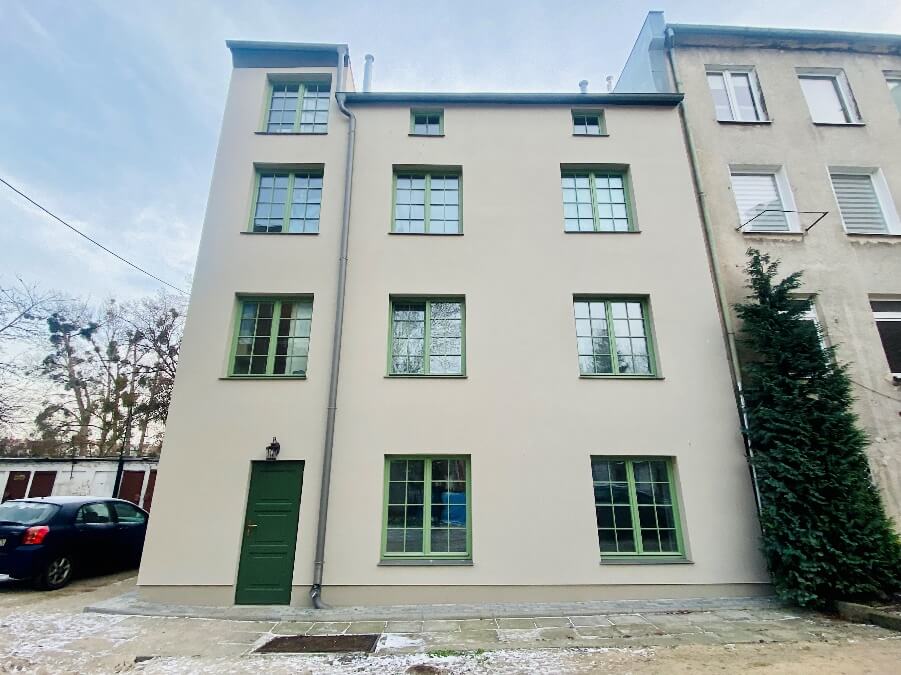 Na zdjęciu tylna elewacja budynku przy ul. Dolna Brama 4 po Rewitalizacji w odcieniu beżu z charakterystyczną zieloną stolarką okienna i drzwiową.