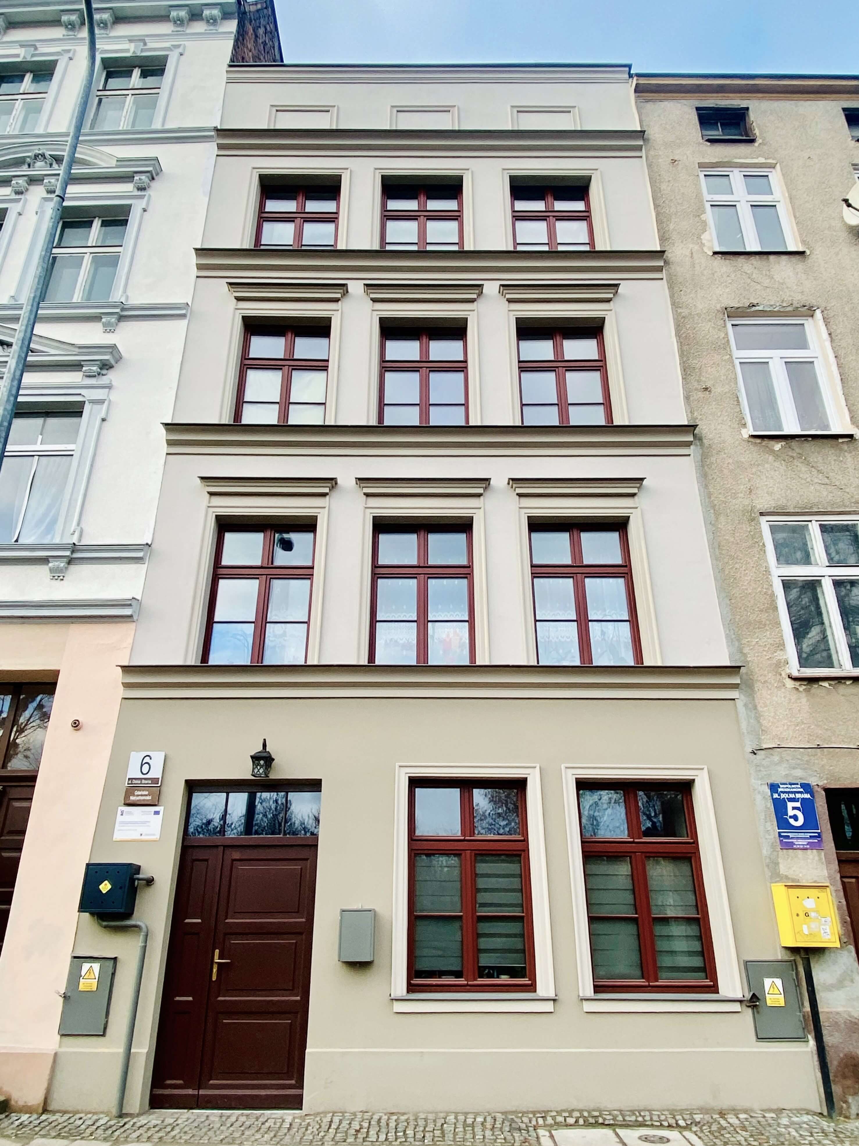 Na zdjęciu frontowa elewacja budynku przy ul. Dolna Brama 6 po Rewitalizacji w odcieniu beżu z charakterystyczną stolarką okienna i drzwiową w odcieniu burgundowym.