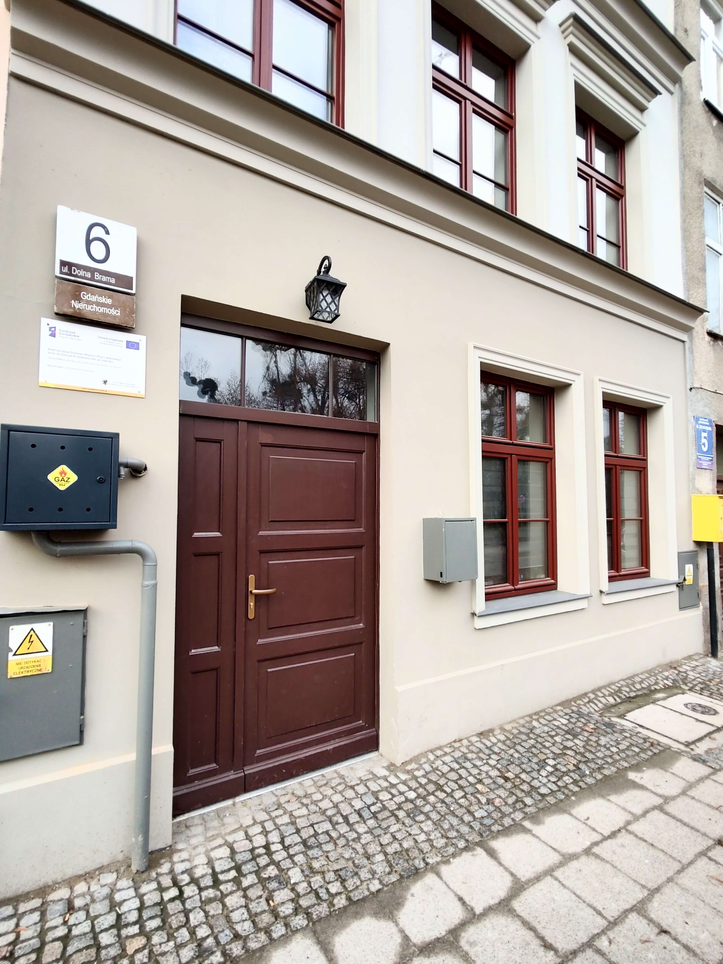 Na zdjęciu frontowa elewacja budynku przy ul. Dolna Brama 6 po Rewitalizacji w odcieniu beżu z charakterystyczną stolarką okienna i drzwiową w odcieniu burgundowym.