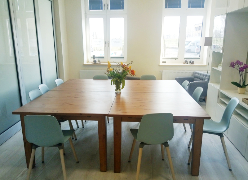 Zdjęcie przedstawia wyremontowane pomieszczenie z przeznaczeniem na potrzeby  fundacji FOSA i Centrum Wsparcia i Terapii Rodzin. Na pierwszym planie duży stół z krzesłami.