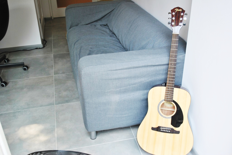 Wnętrze Youth Point - na pierwszym planie znajduje się gitara akustyczna oparta o szarą sofę. 