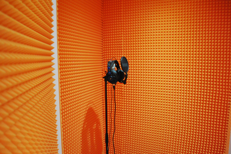zdjęcie przedstawia wyremontowane, nowe studio muzyczne. Ściany studia w intensywnym pomarańczowym kolorze, na środku profesjonalny mikrofon.