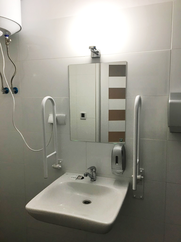 zdjęcie przedstawia wyremontowana toaletę w Youth Point.
                Na pierwszym planie umywalka i lustro oraz urządzenia wspomagające osoby z niepełnosprawnościami. 