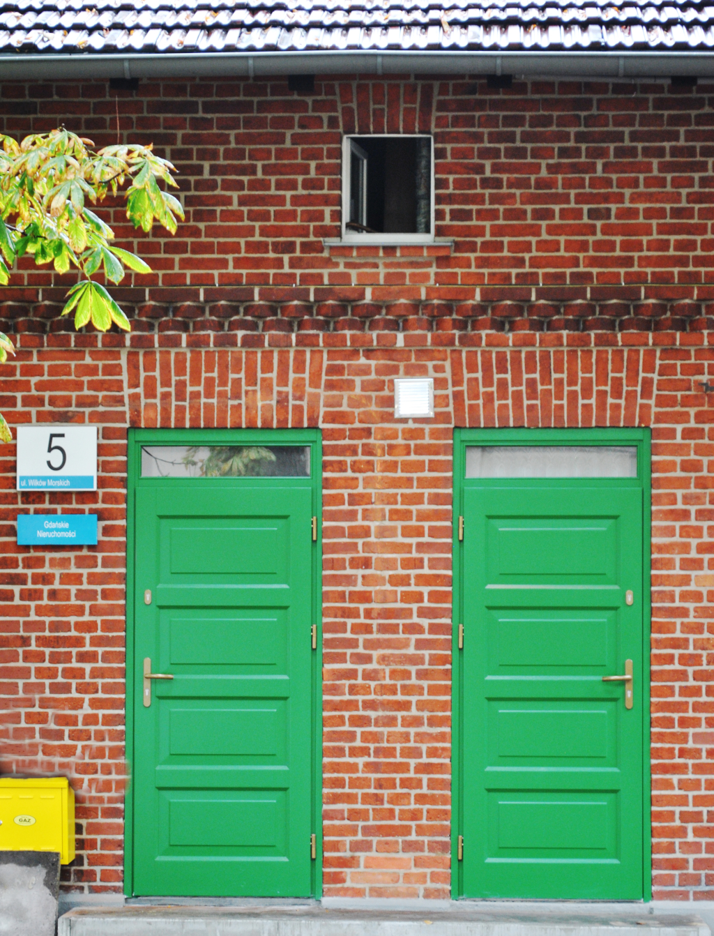 na zdjęciu dwa wejścia do budynku  z tablica numeryczną. W dużym przybliżeniu widoczna, nowa stolarka drzwiowa w kolorze intensywnej zieleni. 