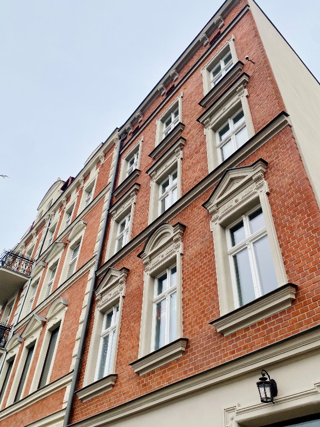 Na zdjęciu ceglana elewacja budynku przy ul. Trakt Św. Wojciecha 101 po Rewitalizacji ze zdobiącymi ją odrestaurowanymi naczółkami.